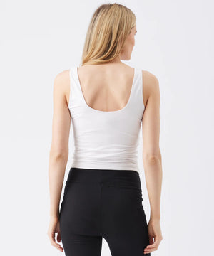 Woman wearing a white tank top and black leggings on a plain background