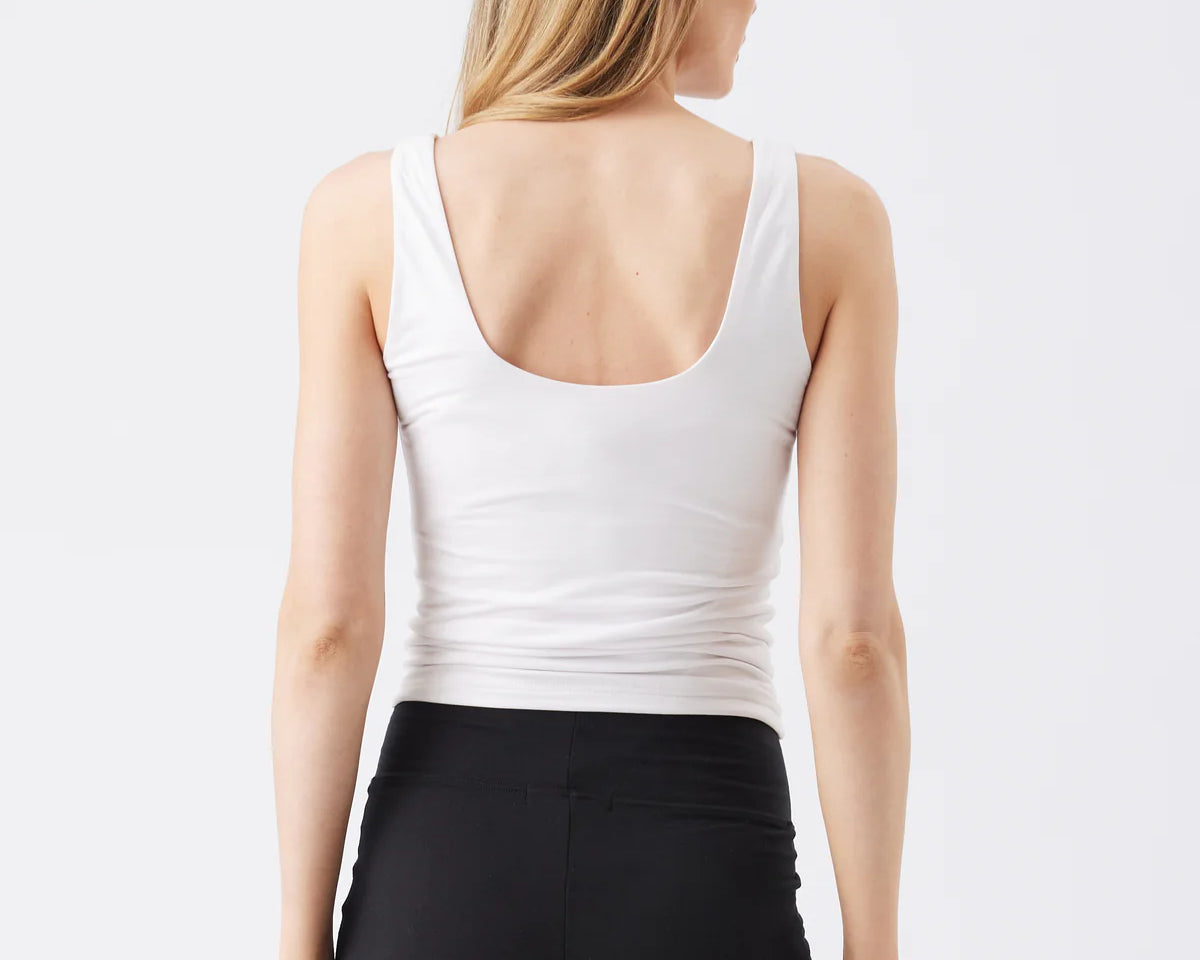 Woman wearing a white tank top and black leggings on a plain background