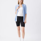 Woman wearing a light blue shirt, white top, black shorts, and white sneakers on a white background