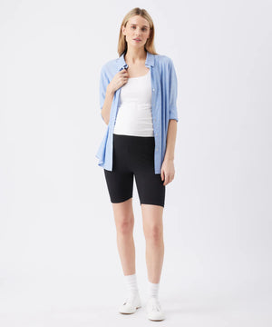 Woman wearing a light blue shirt, white top, black shorts, and white sneakers on a white background
