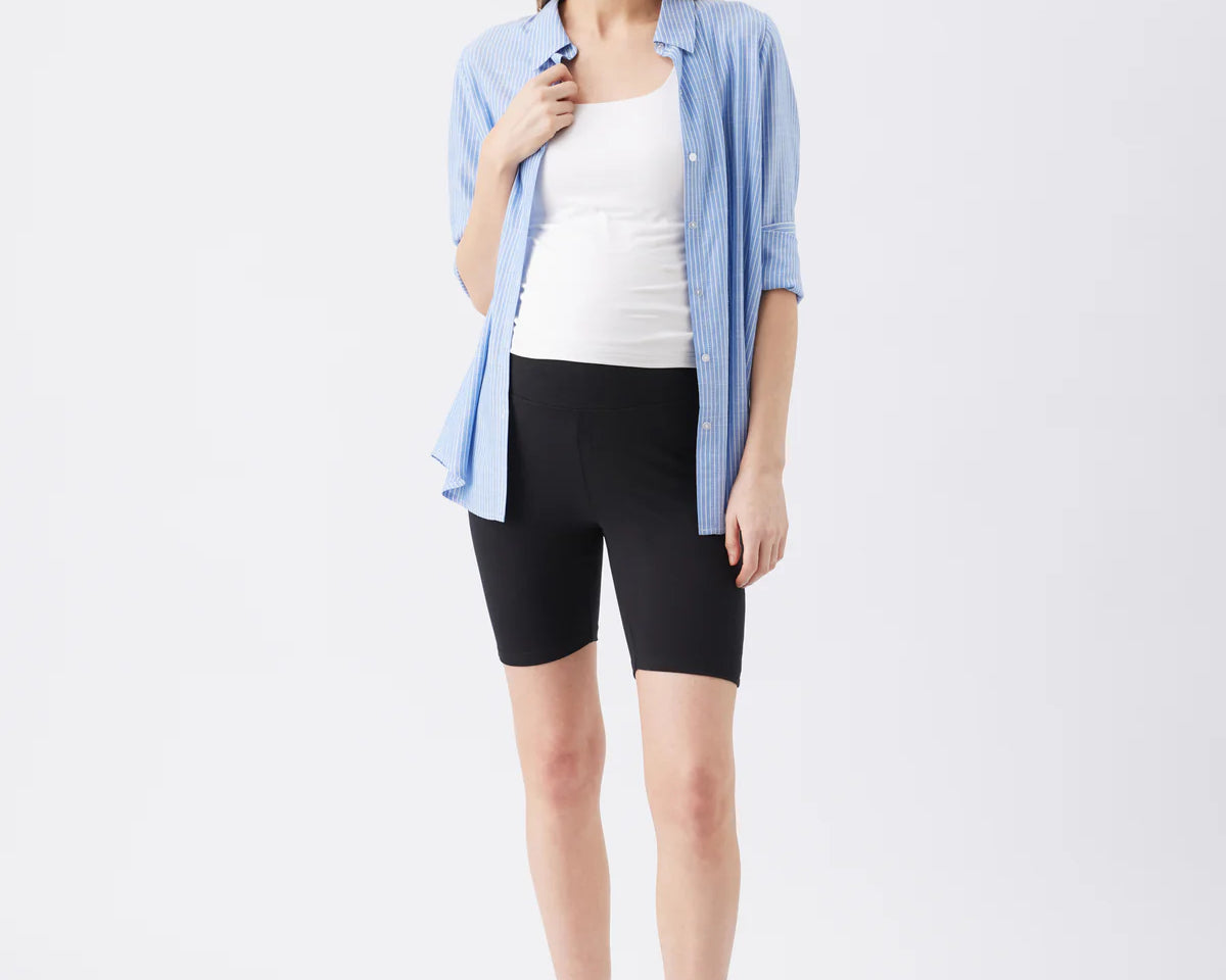 Woman wearing a light blue shirt, white top, black shorts, and white sneakers on a white background