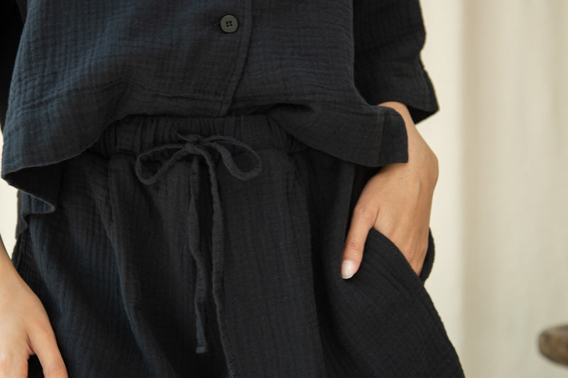 Person wearing a black outfit with shorts and a top, standing against a neutral background.