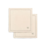 Two square cream-colored cotton napkins with stitched borders and a small bow motif in the lower right corner, stacked on a white background.