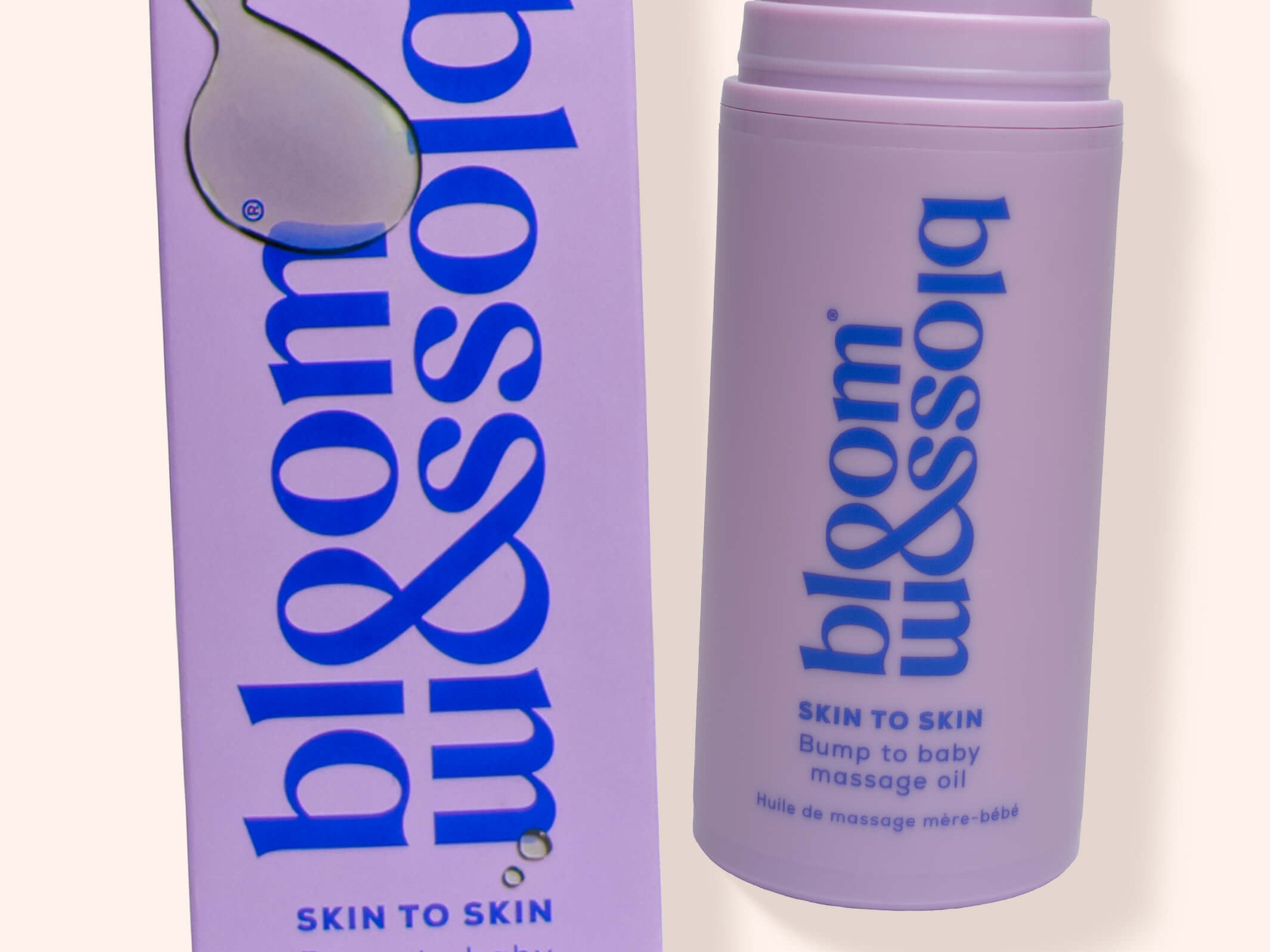 A bottle and box of bloom & blossom Skin to Skin Bump to Baby Massage Oil, shown on a warm off-white background. The packaging is lavender purple with blue text and a white droplet logo.