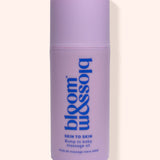 A lavender purple cylindrical bottle of bloom & soft Skin to Skin Bump to Baby Massage Oil, featuring blue text on a clean, solid, light cream background.