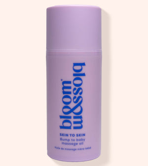 A lavender purple cylindrical bottle of bloom & soft Skin to Skin Bump to Baby Massage Oil, featuring blue text on a clean, solid, light cream background.