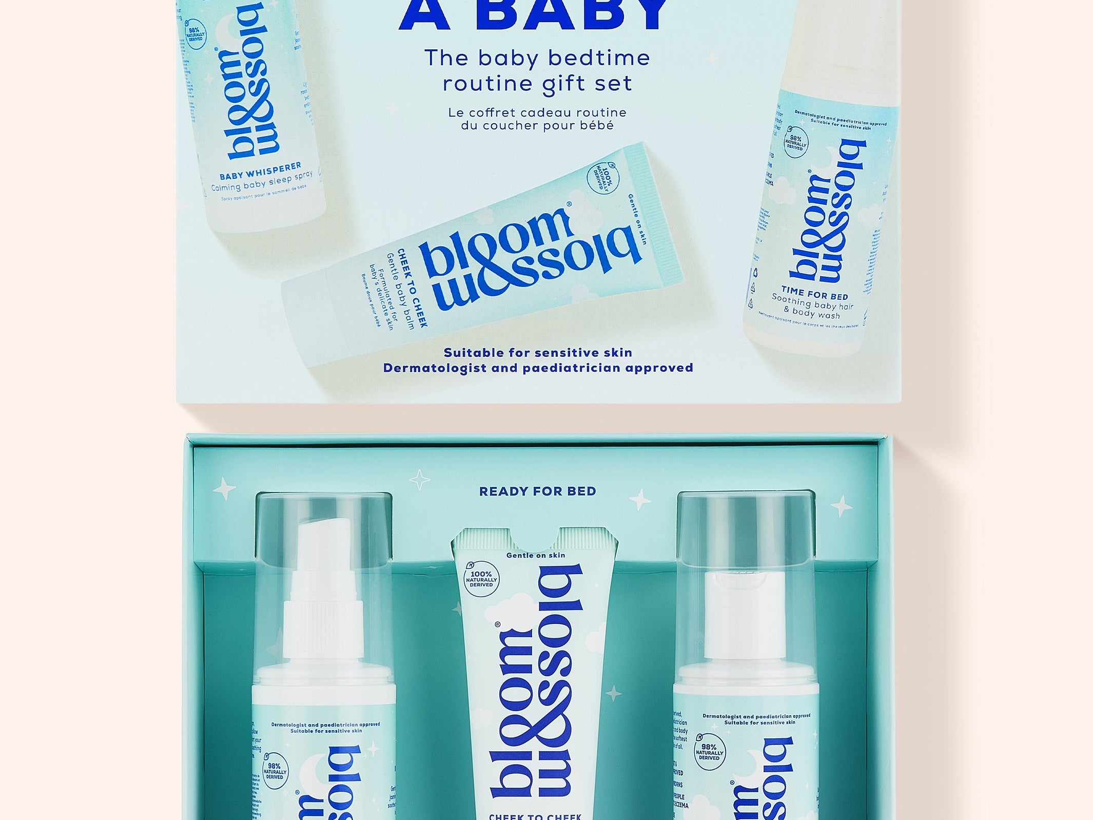 Bloom Blossom Sleep Like a Baby gift set shown open, with the matching light blue outer box above and three skincare items inside: a pump bottle, a tube, and a spray bottle, all in a clean studio-style layout on a pale pink background.