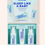 Bloom Blossom Sleep Like a Baby gift set shown open, with the matching light blue outer box above and three skincare items inside: a pump bottle, a tube, and a spray bottle, all in a clean studio-style layout on a pale pink background.
