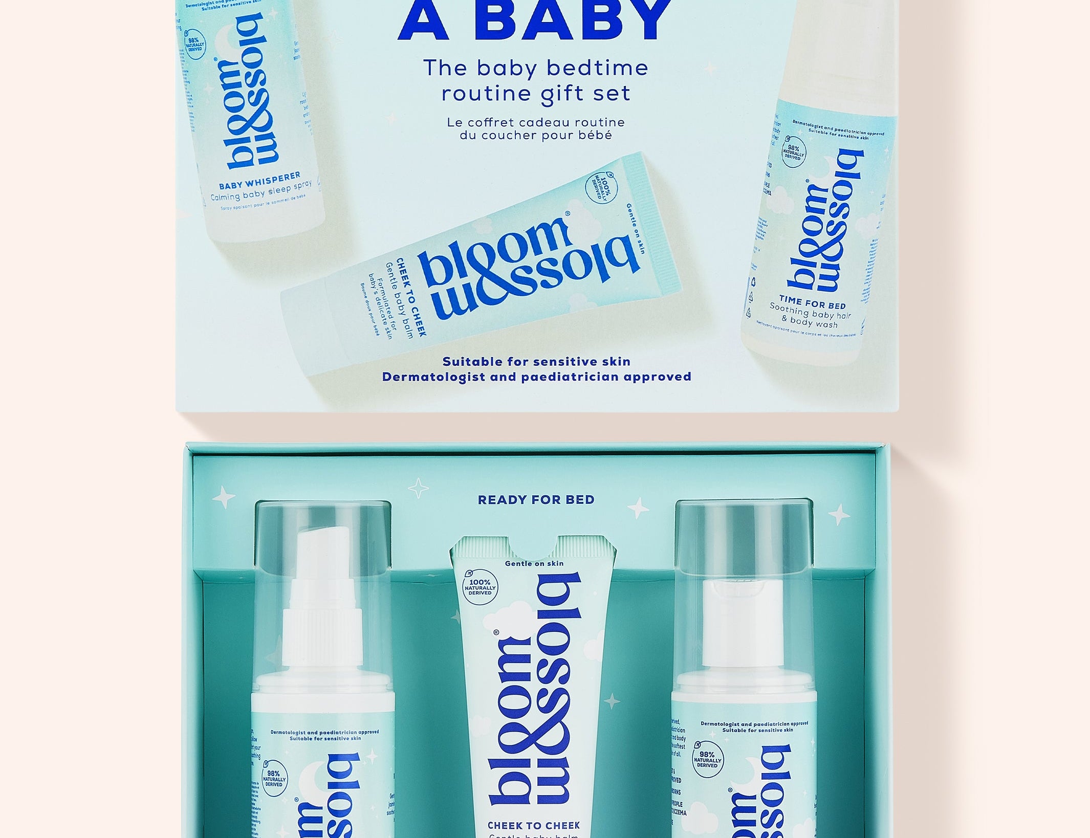 Bloom Blossom Sleep Like a Baby gift set shown open, with the matching light blue outer box above and three skincare items inside: a pump bottle, a tube, and a spray bottle, all in a clean studio-style layout on a pale pink background.