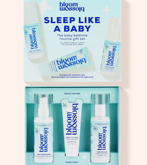 Bloom Blossom Sleep Like a Baby gift set shown open, with the matching light blue outer box above and three skincare items inside: a pump bottle, a tube, and a spray bottle, all in a clean studio-style layout on a pale pink background.