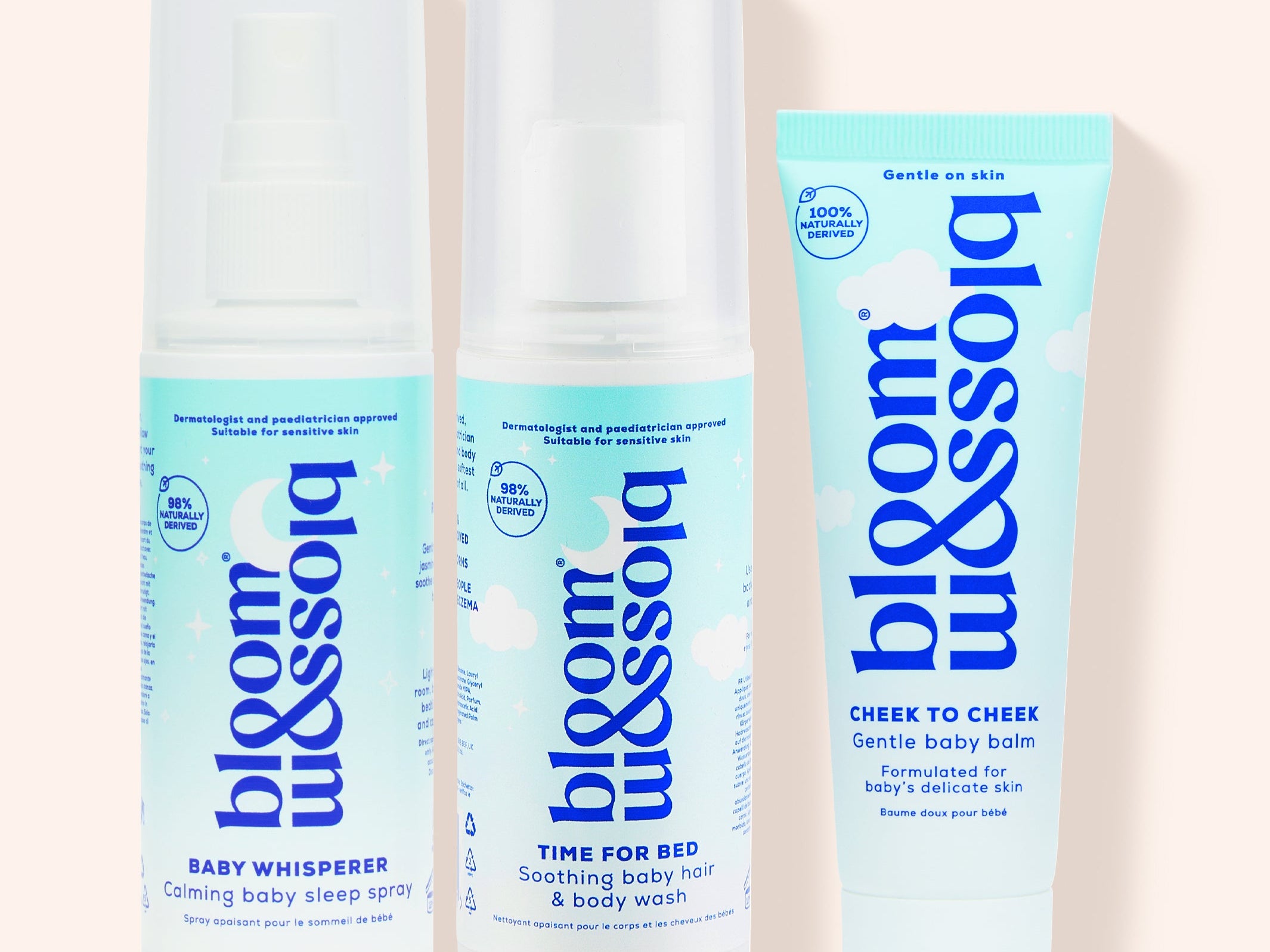 Three Bloom & Soho baby care products arranged on a pale peach background: a Baby Whisperer clinging sleep spray bottle, a Time for Bed soothing baby hair & body wash bottle, and a Cheer to Cheer gentle baby balm tube.
