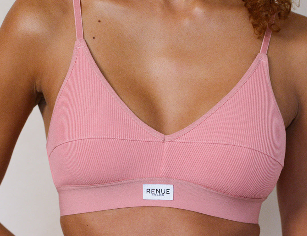 A close-up of a model wearing a ribbed pink sports bra with thin straps and a white brand label reading 'RENUE' on the underband.