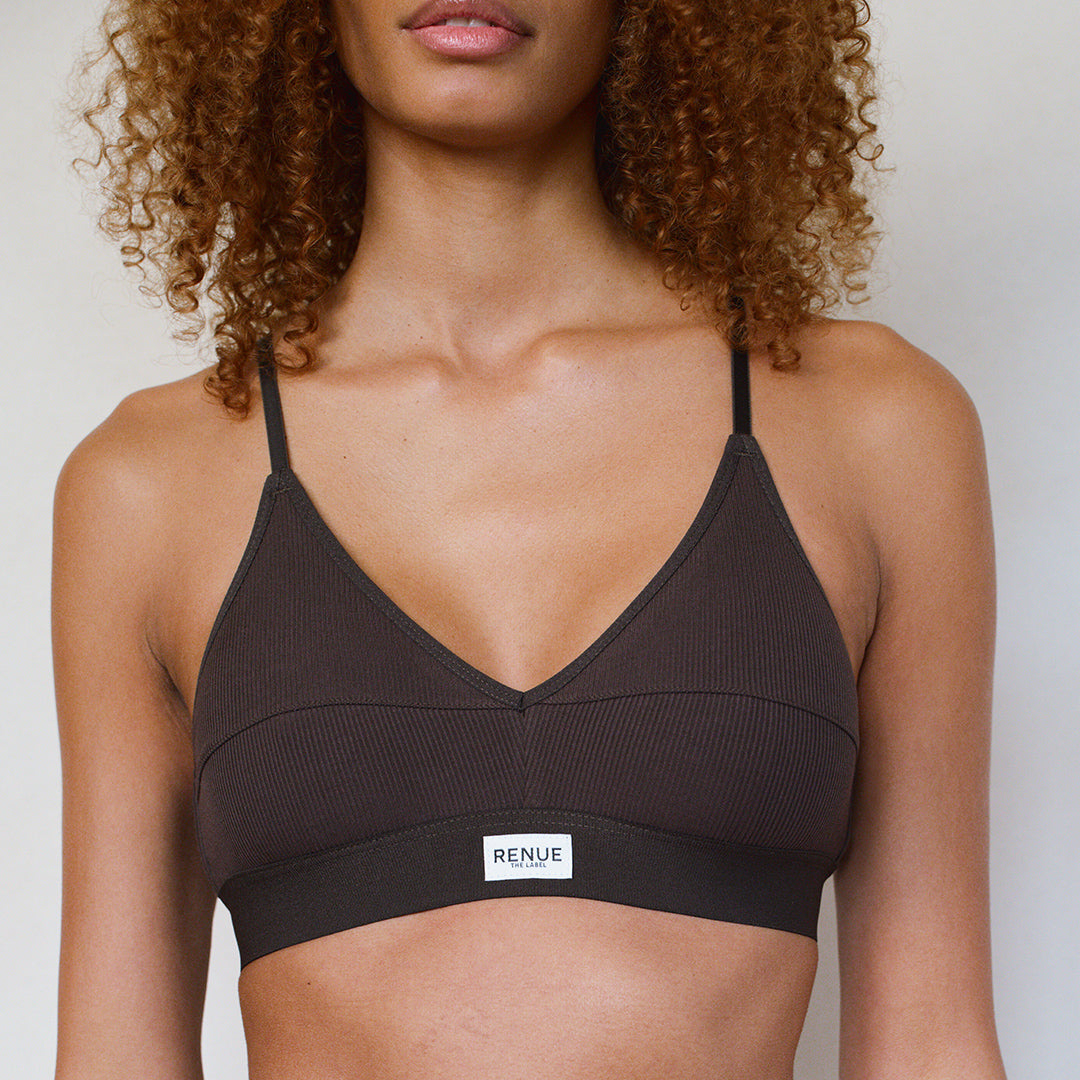 A close-up of a model wearing a dark brown ribbed V-neck bralette with thin straps and a white brand label that reads 'RENUE'.