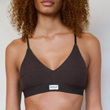 A close-up of a model wearing a dark brown ribbed V-neck bralette with thin straps and a white brand label that reads 'RENUE'.