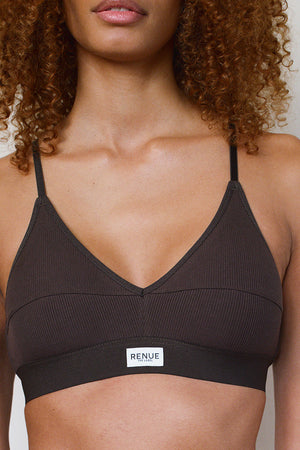 A close-up of a model wearing a dark brown ribbed V-neck bralette with thin straps and a white brand label that reads 'RENUE'.