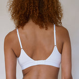 Rear view of a person with curly brown hair wearing a white underwire bra against a plain light background.