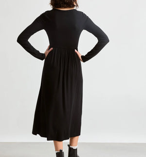A woman shown from the back wearing a black long-sleeve midi dress with a gathered waist, paired with black ankle boots, against a plain light gray studio background.