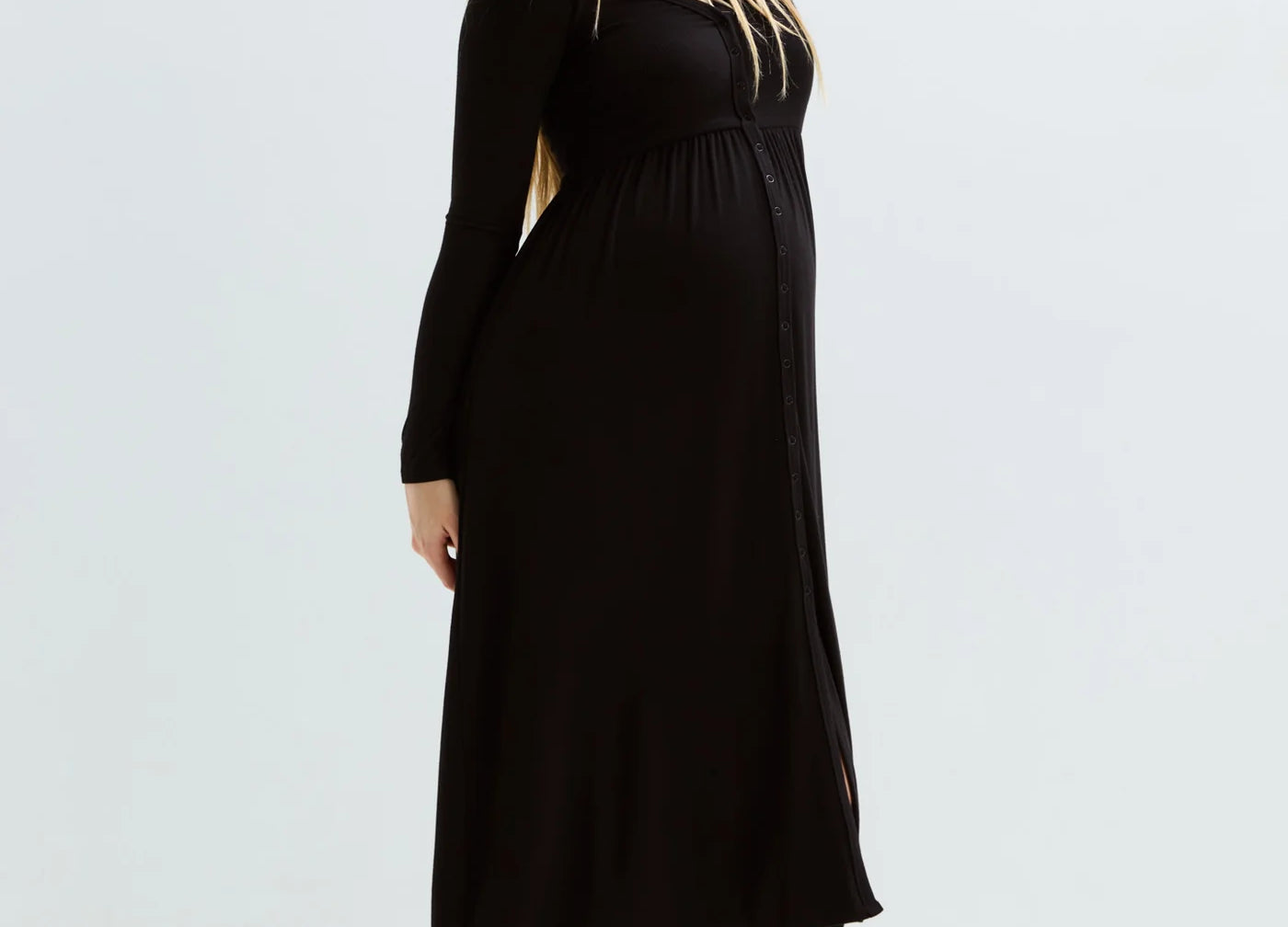 A pregnant woman modeling a black long-sleeve maternity maxi dress, standing barefoot against a clean white studio background.