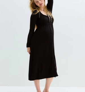 A pregnant woman modeling a black long-sleeve maternity maxi dress, standing barefoot against a clean white studio background.