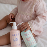Child holding two bottles of Softie baby products on a bed