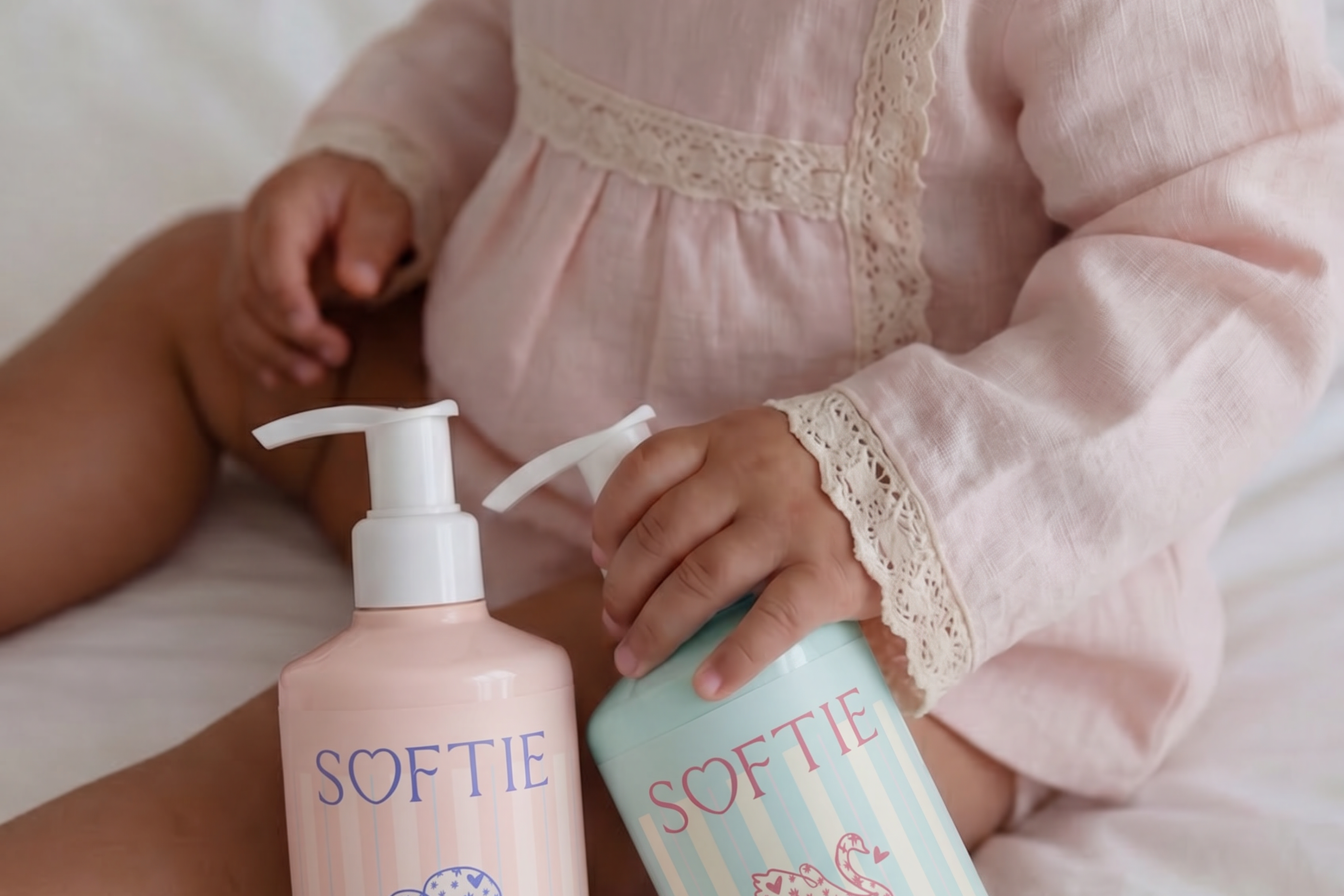 Child holding two bottles of Softie baby products on a bed