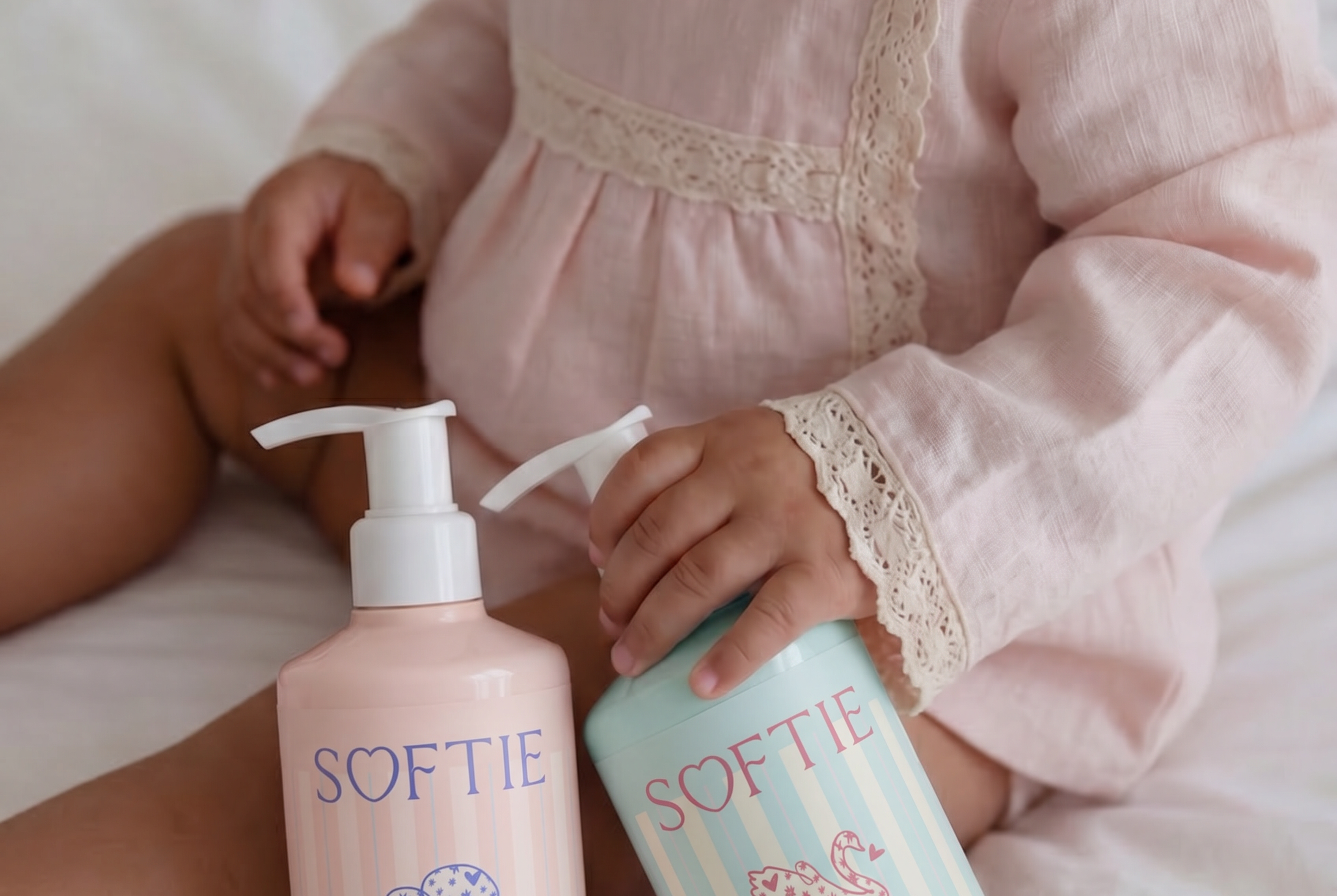 Child holding two bottles of Softie baby products on a bed