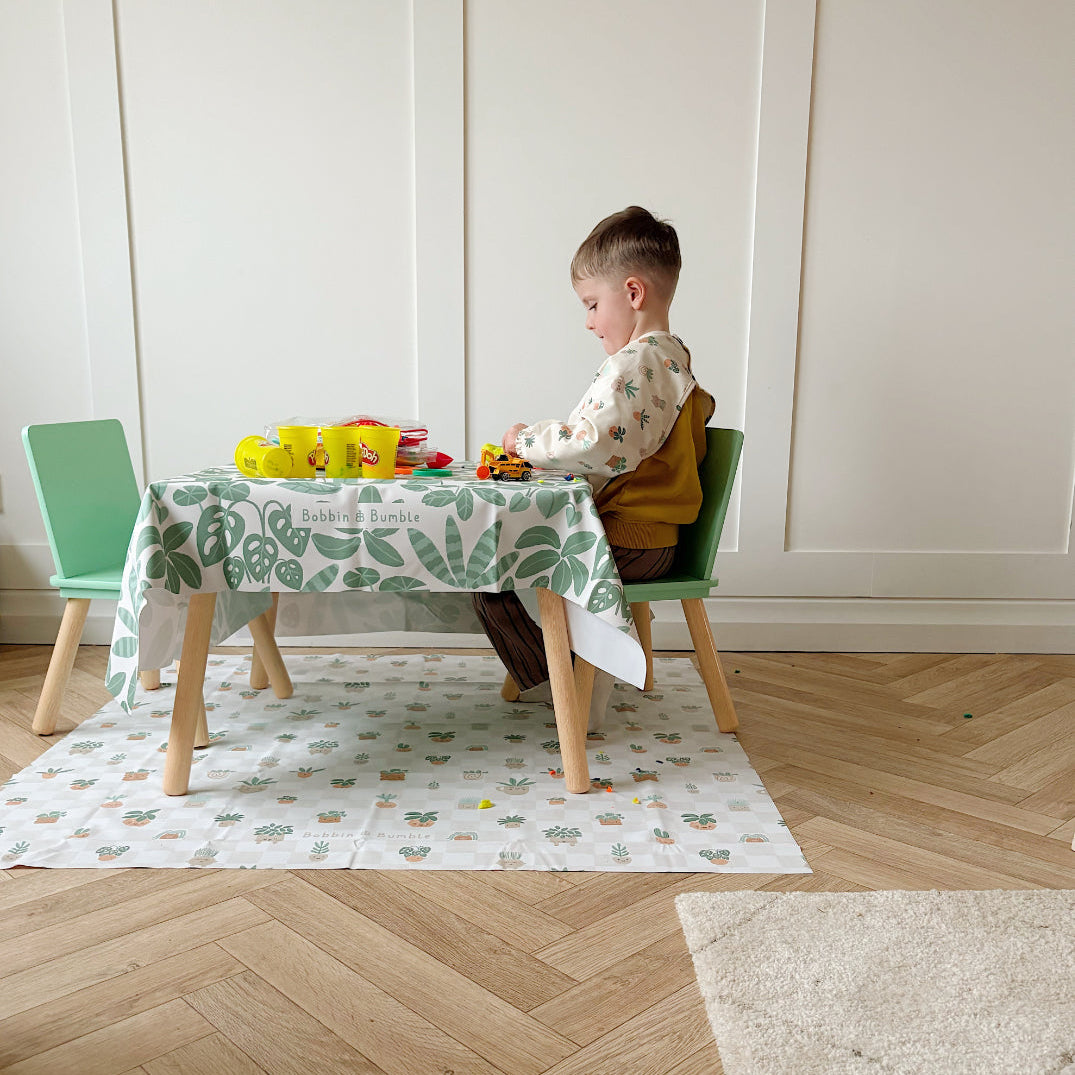 Child-size table and green chairs with the Pot Plants splash mat on the floor and a matching leaf print mat as the tablecloth