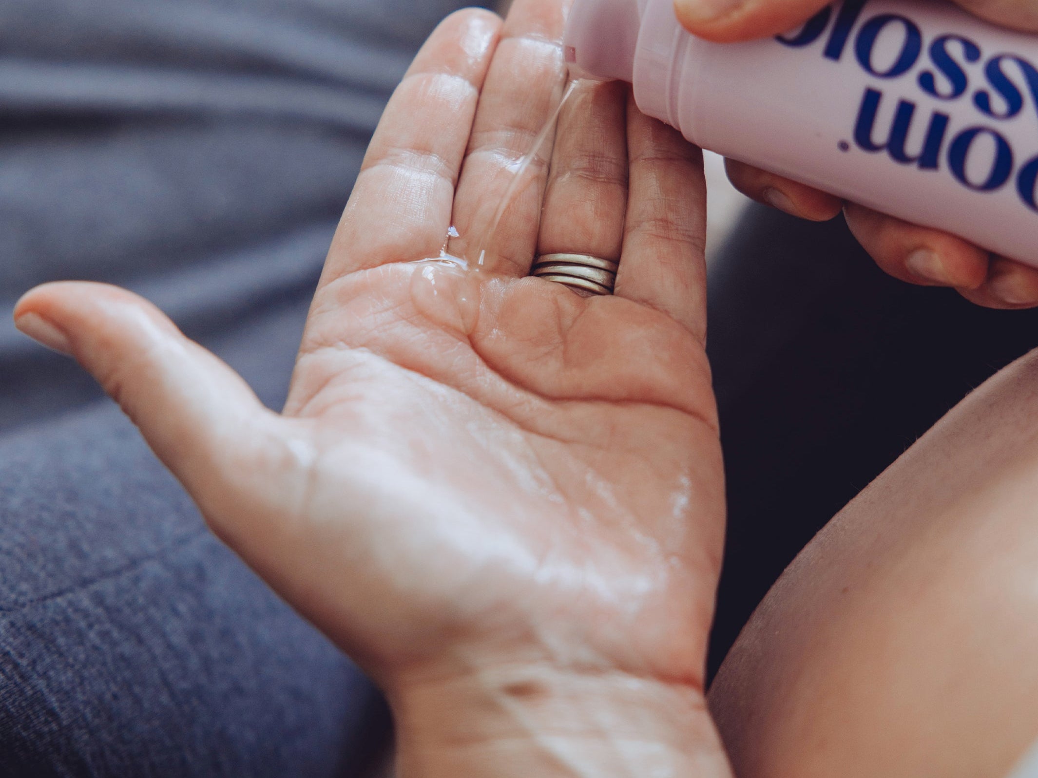 A close-up of a person pouring a clear liquid from a pink bottle labeled 'blossom wood' onto the back of their hand.