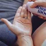 A close-up of a person pouring a clear liquid from a pink bottle labeled 'blossom wood' onto the back of their hand.