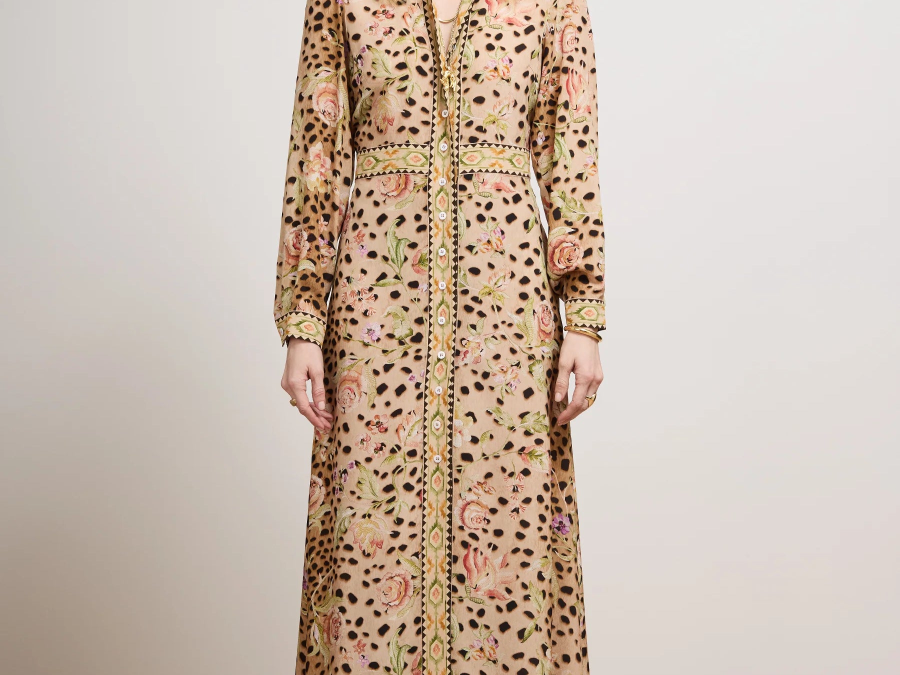 A model stands in a studio wearing a long-sleeved maxi shirt dress with a beige base, black leopard spots, and a pink and green floral pattern, paired with a matching belt and black shoes.