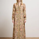 A model stands in a studio wearing a long-sleeved maxi shirt dress with a beige base, black leopard spots, and a pink and green floral pattern, paired with a matching belt and black shoes.