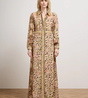 A model stands in a studio wearing a long-sleeved maxi shirt dress with a beige base, black leopard spots, and a pink and green floral pattern, paired with a matching belt and black shoes.