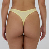 Rear view of a model wearing a pale yellow mesh thong with solid yellow trim, shown against a light gray studio background.
