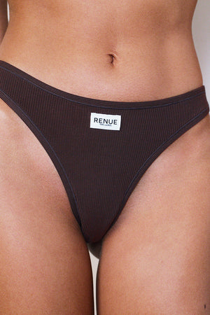 A close-up of a model wearing a dark brown ribbed bikini bottom with a white rectangular brand label that reads 'RENUE'.