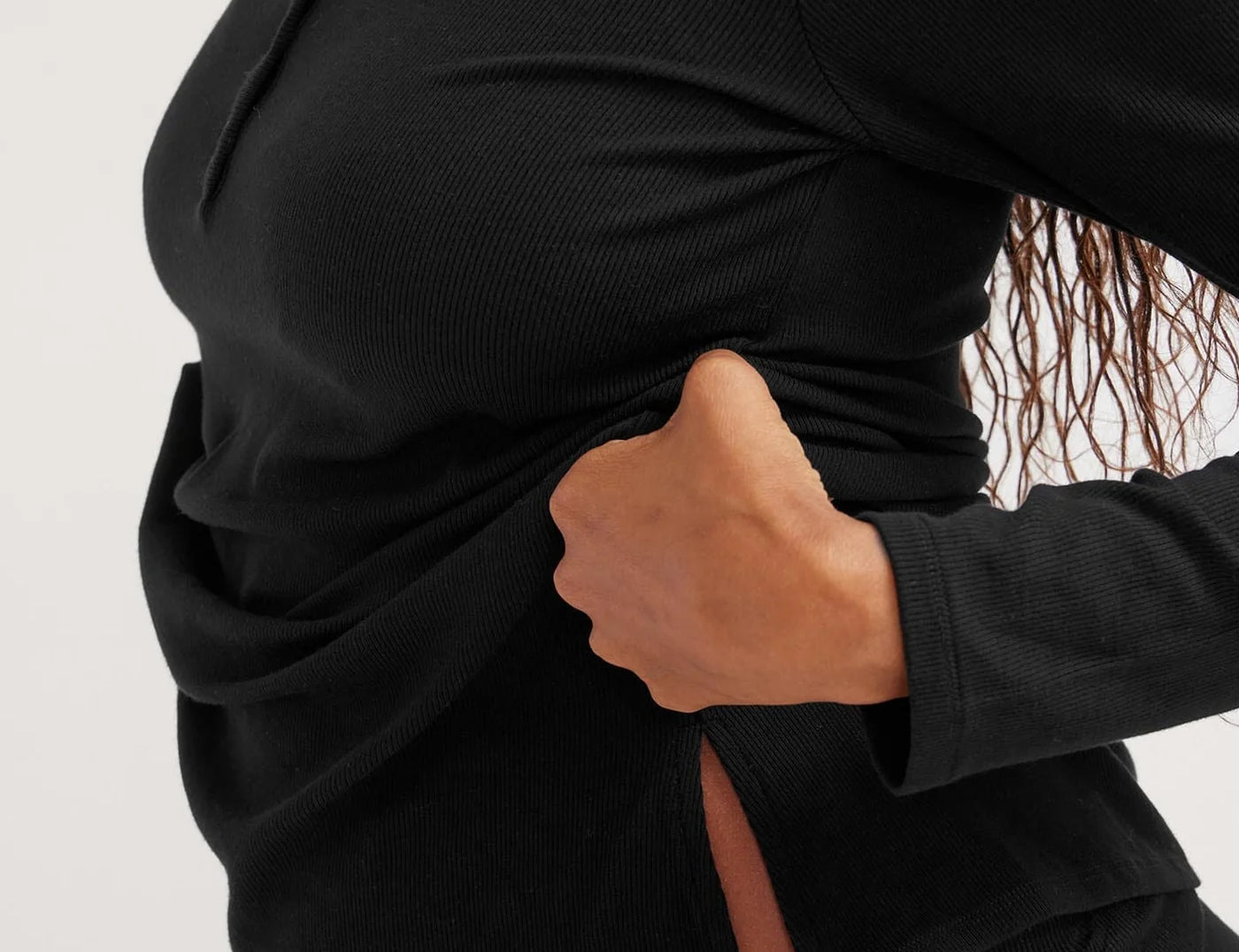 Person wearing a black long-sleeve top with a front slit on a white background