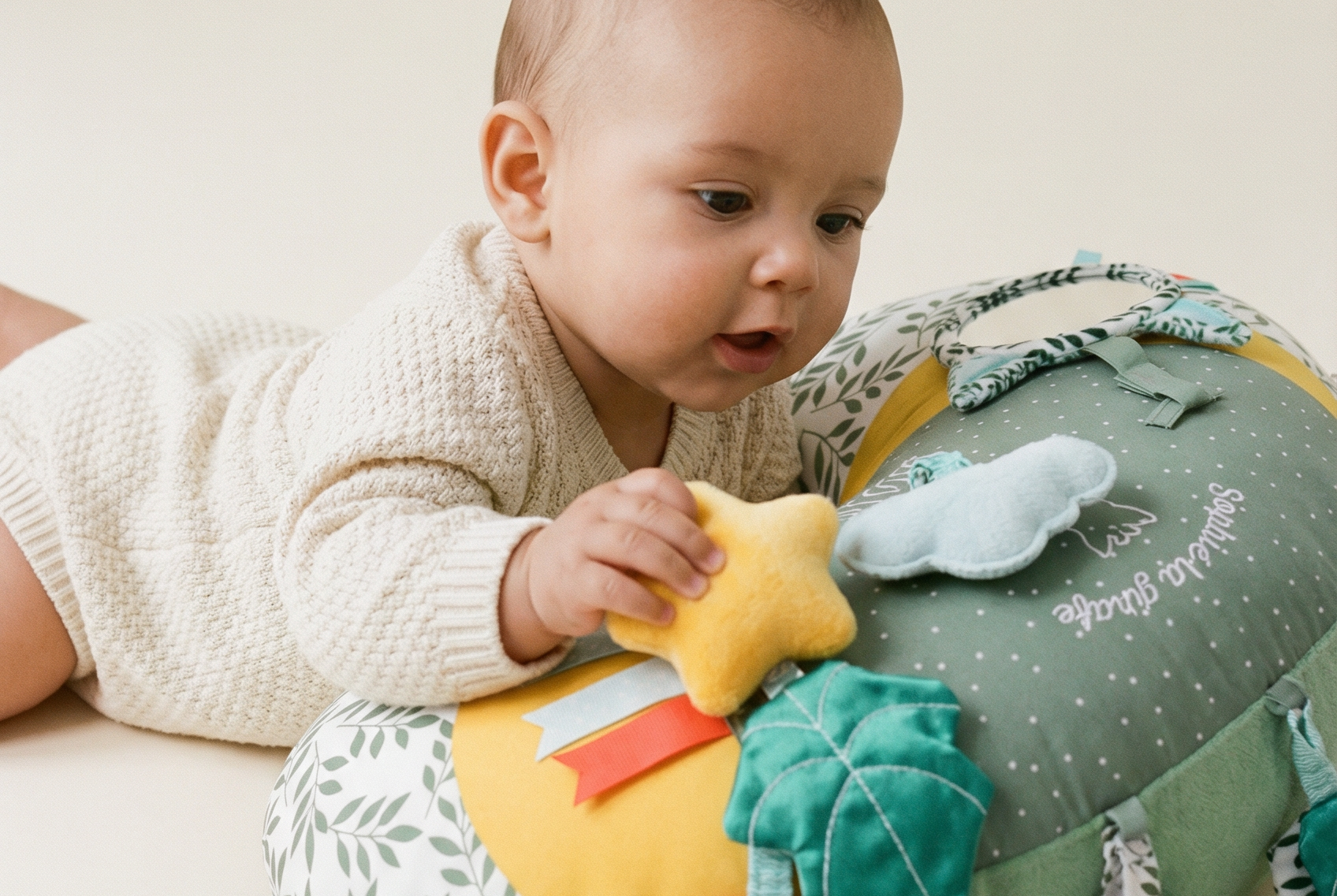 Sophie la girafe Cosy Play Cushion, baby lying on tummy over the cushion and holding the yellow star toy