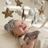 Safari Dreams Felt Cot Mobile hanging over a smiling baby lying on a cot, reaching up towards the felt rhino