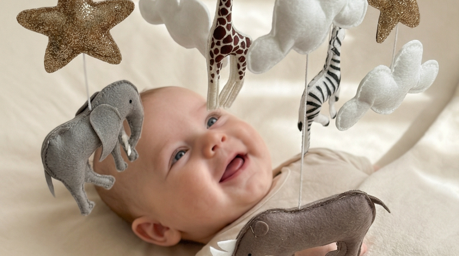 Safari Dreams Felt Cot Mobile hanging over a smiling baby lying on a cot, reaching up towards the felt rhino