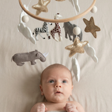 Safari Dreams Felt Cot Mobile above a wide-eyed baby lying on a bed, with the felt animals, stars and moon hanging