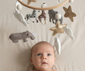 Safari Dreams Felt Cot Mobile above a wide-eyed baby lying on a bed, with the felt animals, stars and moon hanging