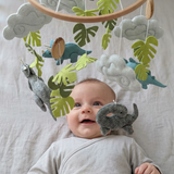 Little Dino Land felt cot mobile hanging over a smiling baby lying on their back in a cot