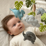 Little Dino Land felt cot mobile with a baby gazing up at the hanging blue and grey dinosaurs and clouds