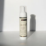 Lusso Tan tinted self tanning mousse, Dark shade bottle with pump top against a white wall with a soft shadow