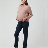 Pregnant woman wearing a pink sweater and navy pants on a white background