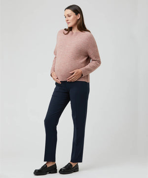 Pregnant woman wearing a pink sweater and navy pants on a white background