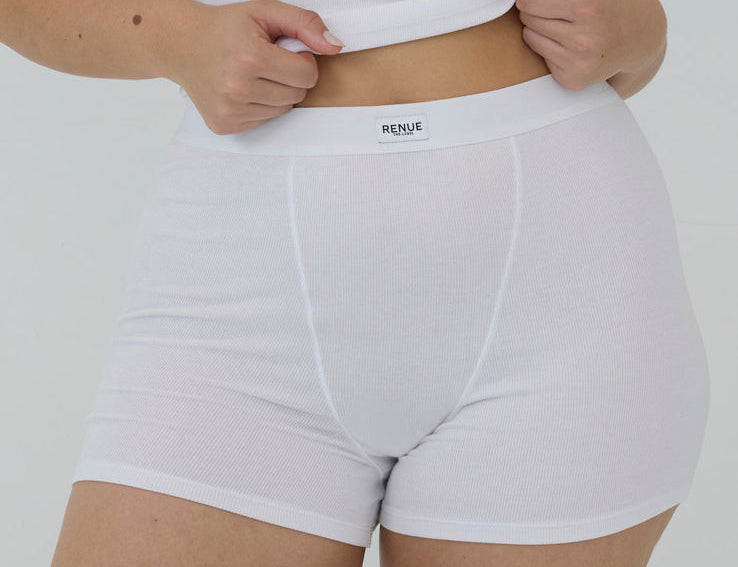 A close-up of a model wearing white ribbed high-waisted briefs with a visible waistband label reading 'RENUE'.