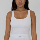 A woman wearing a white ribbed scoop-neck tank top and matching white bottoms, shown from the waist up against a light gray studio background. The brand name 'RENUE' is visible on the waistband label.