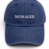 A navy blue washed cotton baseball cap with the word 'MOMAGER' embroidered in white serif letters across the front, shown against a plain white background.