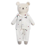 A plush teddy bear wearing a cream-colored pajama set with a small red berry and green holly print, set against a plain white background.
