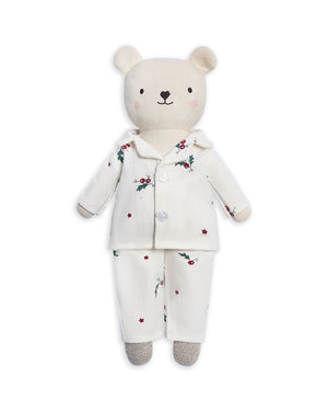 A plush teddy bear wearing a cream-colored pajama set with a small red berry and green holly print, set against a plain white background.